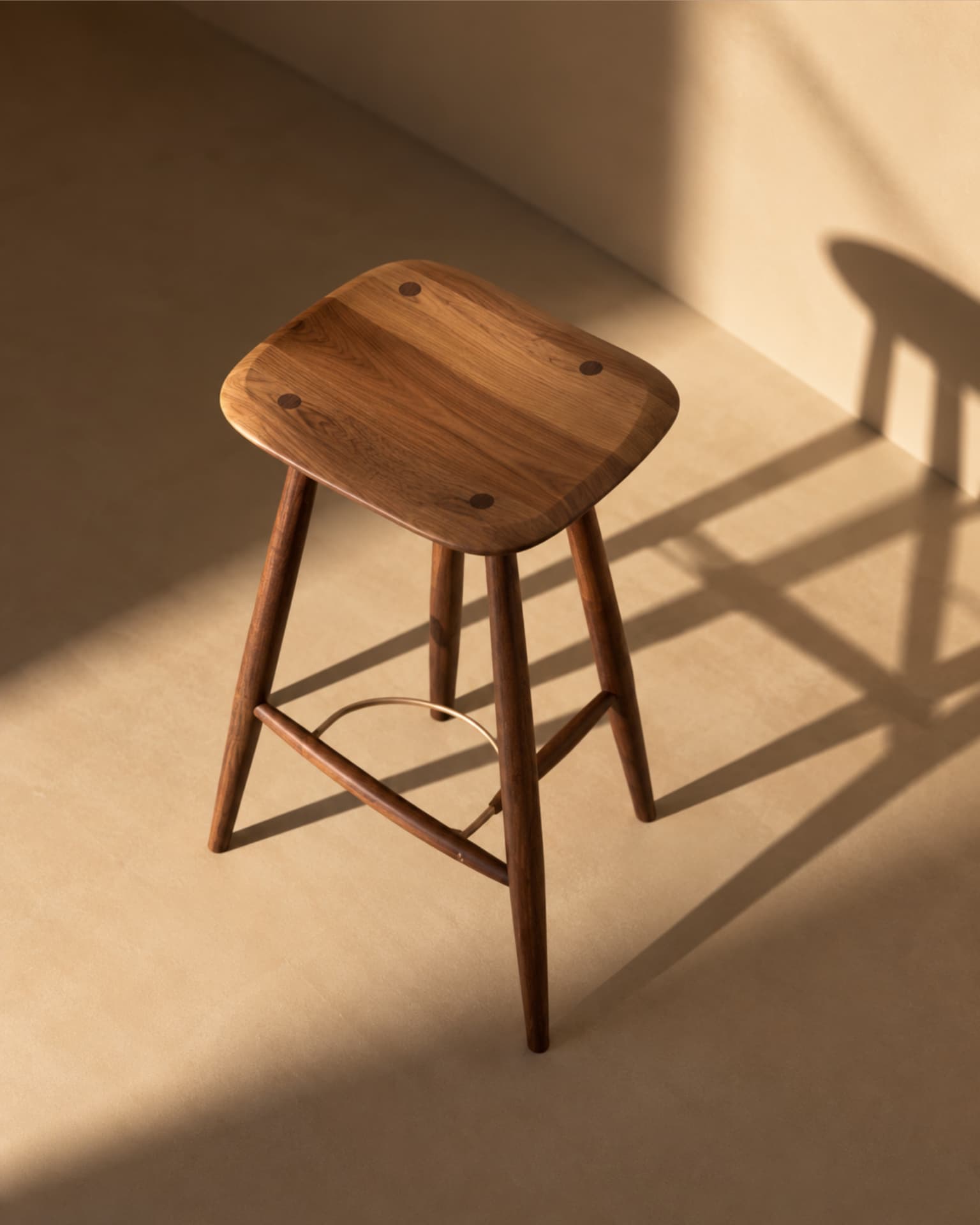 Three-quarter view of a walnut wooden stool with brass footrest